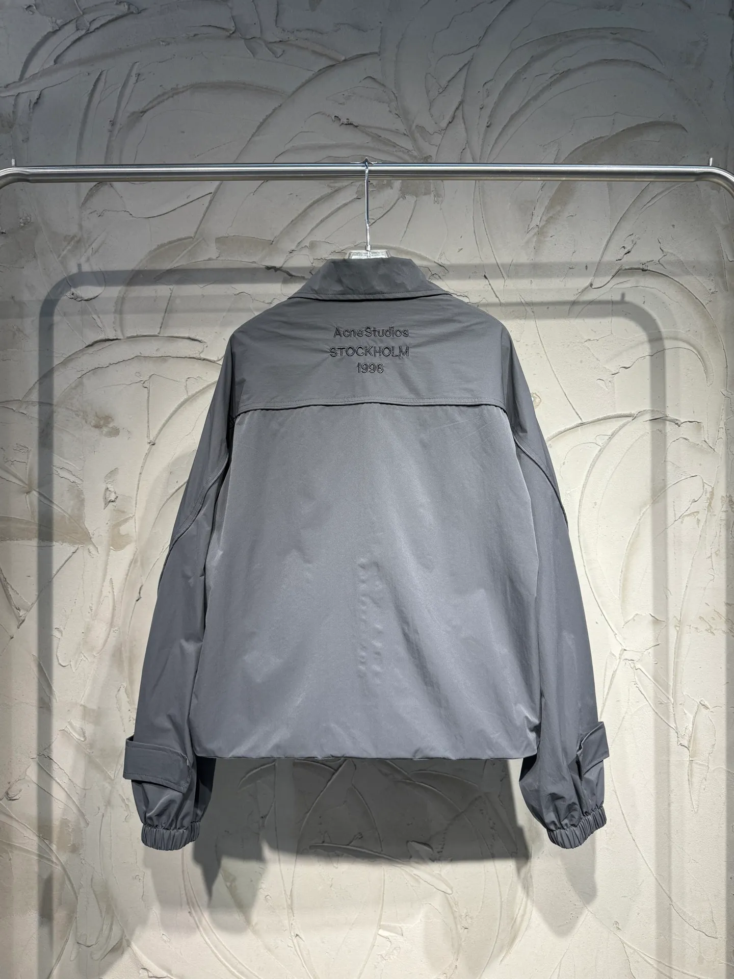 Acne Studios 26SS Large Lapel Short Jacket The fabric is made of 100% nylon (nylon/polyamide fiber) 75D high-density wrinkled nylon. The fabric has been permanently pressed and shaped by high temperature, and washed with high-pressure wrinkles at the factory to form its own irregular texture, permanently retaining the wrinkled texture, which will not disappear after washing. Matte matte coating removes the plastic glossy surface of nylon itself to create a low-key matte paper feel. Three-proof micro-coating, weak waterproof, anti-fouling, anti-static treatment, not easy to get dust. The interior is made of full-width mesh Breathable nylon lining, which reduces the stickiness of the nylon fabric to the body, improves air circulation, prevents sweating from sticking to the skin, and the zipper does not rub against the skin. The version adopts the raglan split topstitching process, and the front and rear panels are divided diagonally to expose even stitching. The three-dimensional dropped shoulders are loose and the fit is increased to increase the margin of movement. The back neckline is three-dimensional and high-density computer embroidered, and the embroidery lines are dense and not prickly. Customized all-metal matte nylon zipper, Genuine Leather embossed brand letters on the zipper leather tab, zipper tape with same color nylon fit to the body, double-locked reinforcement on both sides of the zipper to prevent pulling and tearing. Color: Gray Size: S M L